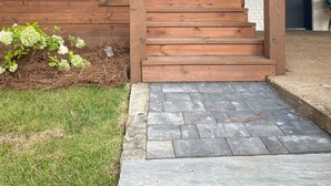 A wooden staircase leading to a house with a stone pathway and a grassy area.