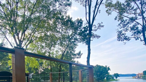 A wooden deck overlooking a lake with a grassy area and a building in the distance.