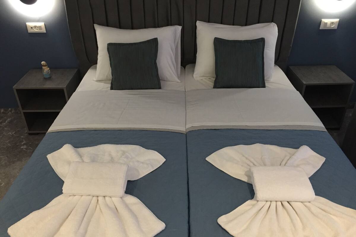 A double bed with white and dark green pillows, two bedside tables, and a nightstand with a bottle.