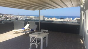 Eine Dachterrasse mit Tisch und Stühlen, einem überdachten Bereich und Blick auf Stadt und Meer.
