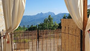 A covered patio with a view of mountains, bamboo fencing, and a stone wall. - 3 Bedroom Village House with Private Pool in Garfagnana - restaurant nearby (Comune di Villa Collemandina)