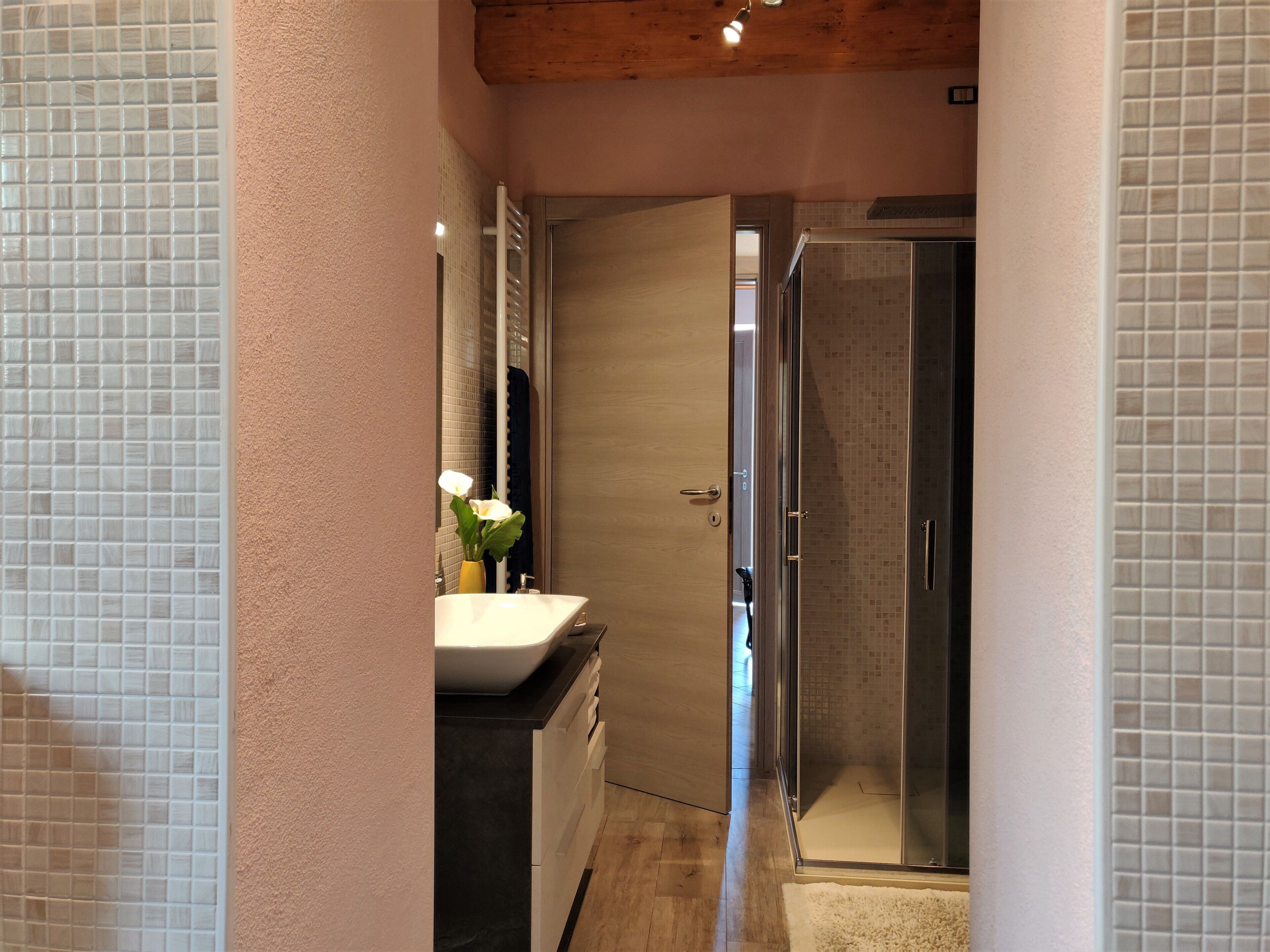 Un baño estrecho con lavamanos blanco, espejo y zona de ducha.