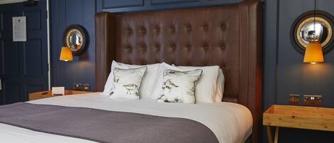 Un dormitorio con cabecera capitonada, una cama grande con ropa de cama blanca, dos lámparas de pared y una mesita de noche de madera.