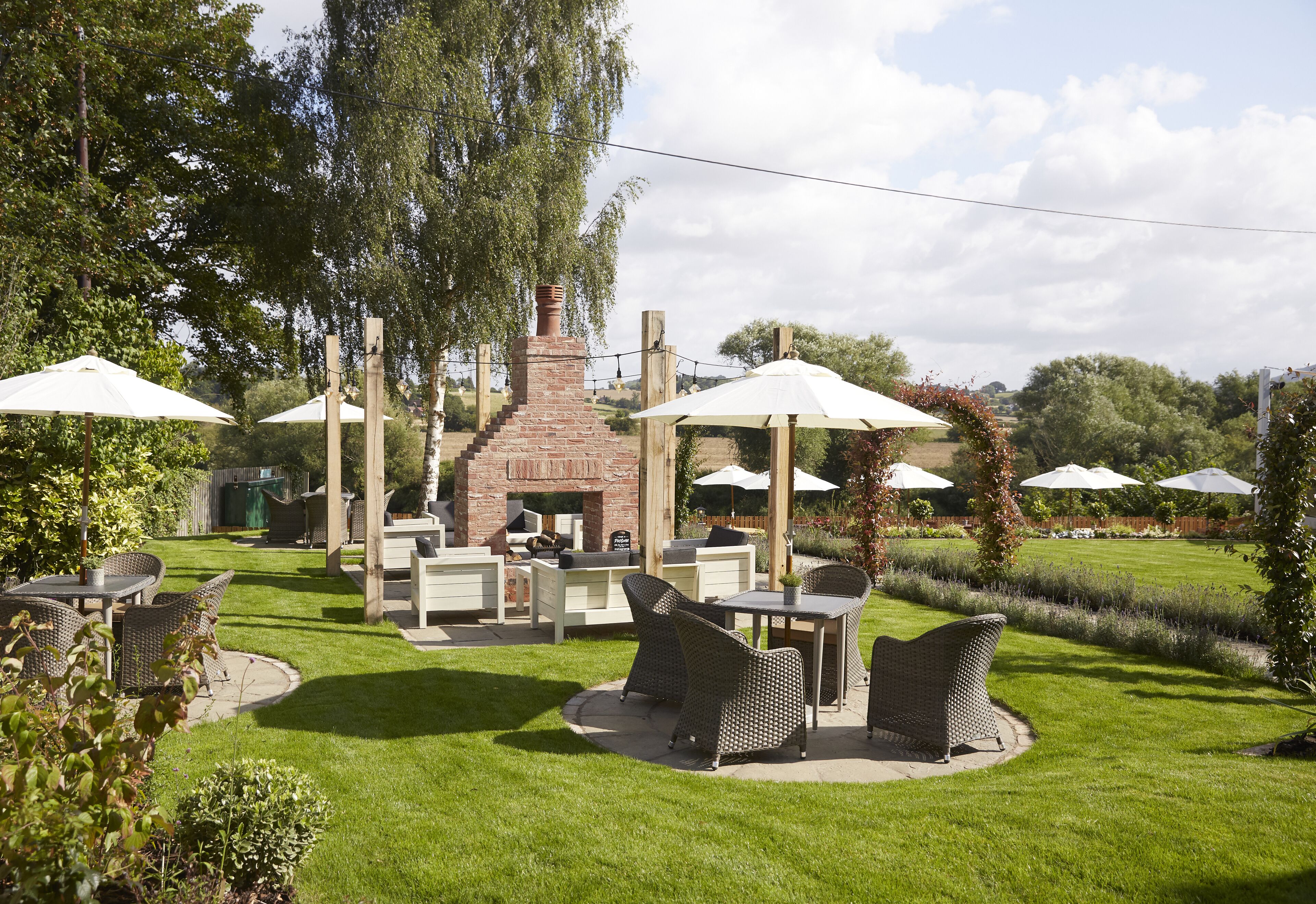 An outdoor patio area with wicker furniture, a brick fireplace, and white umbrellas.
