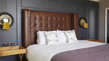 Un dormitorio con cabecera capitonada, mesita de noche de madera, cama con ropa de cama blanca y dos lámparas fijadas a la pared.