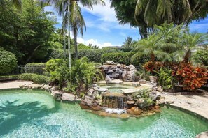 Une piscine agrémentée d’une cascade et entourée d’une végétation tropicale.