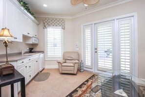 A living room with a beige armchair, a glass coffee table, a lamp, a fireplace, and a large window with blinds. - Captiva Tarpon (Captiva)