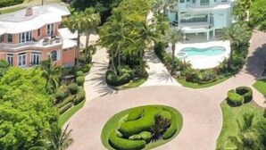 Una casa grande de varios pisos con piscina, rodeada de exuberante vegetación y vistas al mar.