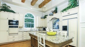 Una cocina con armarios blancos, encimera de granito y una isla central con un frutero de plátanos.