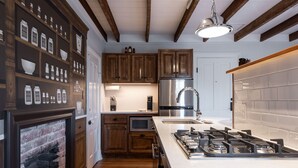 A kitchen with wooden cabinets, a gas stove, a stainless steel refrigerator, and a brick fireplace. - Pharmacy Apartment | Luxury Monthly Stay Downtown (Charlottesville)