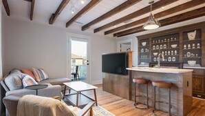 A modern living room with a sofa, coffee table, and a TV. There is a kitchen area with bar stools and a countertop. - Pharmacy Apartment | Luxury Monthly Stay Downtown (Charlottesville)