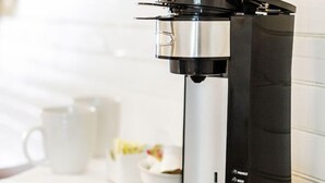 Une machine à café posée sur un comptoir en bois, avec un mur recouvert de carreaux blancs en arrière-plan.