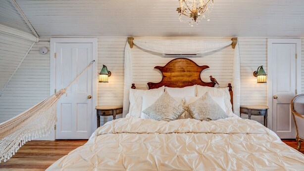 Une chambre spacieuse avec un grand lit, une tête de lit en bois, deux tables de chevet, une chaise et un hamac.