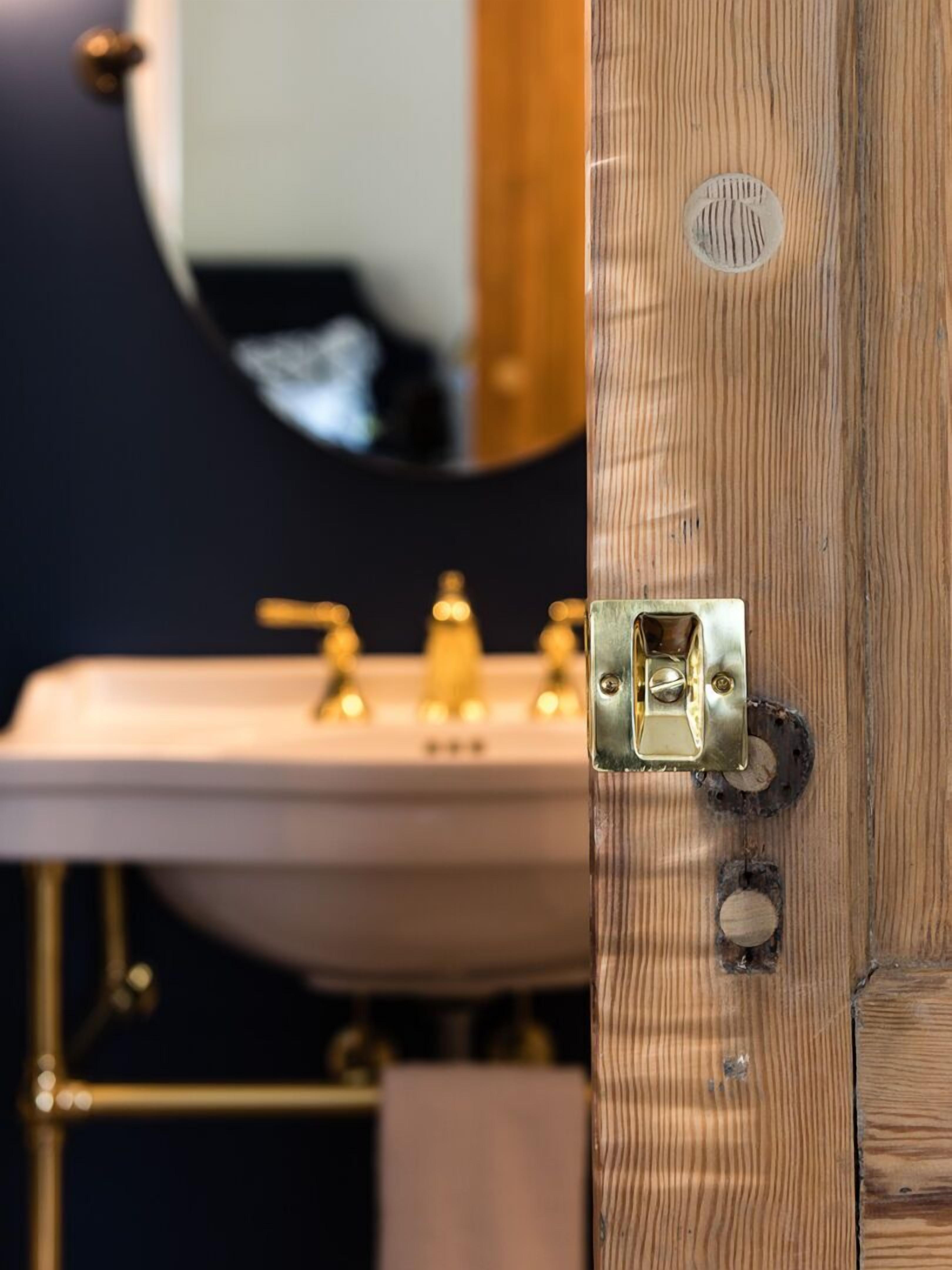 A bathroom with a wooden door, a sink with gold faucets, and a mirror.