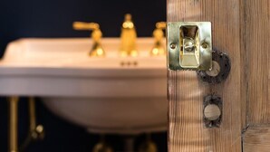 A bathroom with a wooden door, a sink with gold faucets, and a mirror. - Southern Luxury Apartment | Downtown Charlottesville | 30 Night Minimum (Charlottesville)