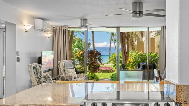 Una cocina con una isla grande, un ventilador de techo y vistas al océano a través de puertas corredizas de vidrio.