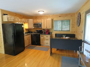 Compact kitchen with a black refrigerator, microwave, and stove, along with a sink and wooden cabinetry.