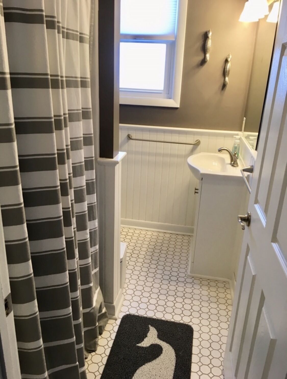 A bathroom with a striped shower curtain, a white sink, a mirror, and a hexagonal tile floor.
