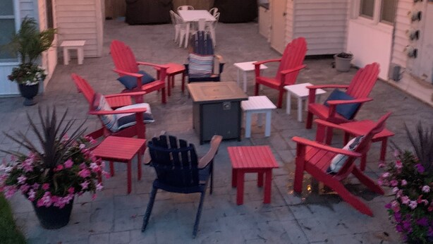 Een terras buiten met rode Adirondack-stoelen, een tafeltje en lichtjes.
