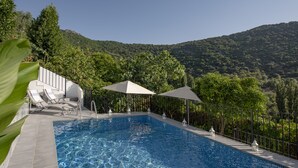 A swimming pool with lounge chairs and umbrellas, surrounded by lush greenery and a mountainous backdrop. - Beautiful House With Fantastic Views of the Sierra (Grazalema)