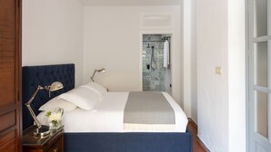 A neatly made bed with a headboard, a bedside table with a lamp, and a bathroom visible through an open door. - Beautiful House With Fantastic Views of the Sierra (Grazalema)