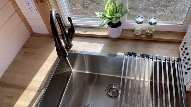 A stainless steel sink with a modern faucet, a potted plant, and two containers on a wooden window sill. - Tiny House in the country, close to Billings (Worden)