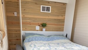 A bedroom with a wooden headboard, a bed with a quilt, a bench, and a small plant. - Tiny House in the country, close to Billings (Worden)