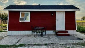 A small red building with a white door, a window, and a table with chairs outside. - Tiny House in the country, close to Billings (Worden)