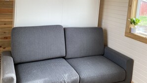 A grey sofa in a room with wooden walls and a ceiling fan. - Tiny House in the country, close to Billings (Worden)