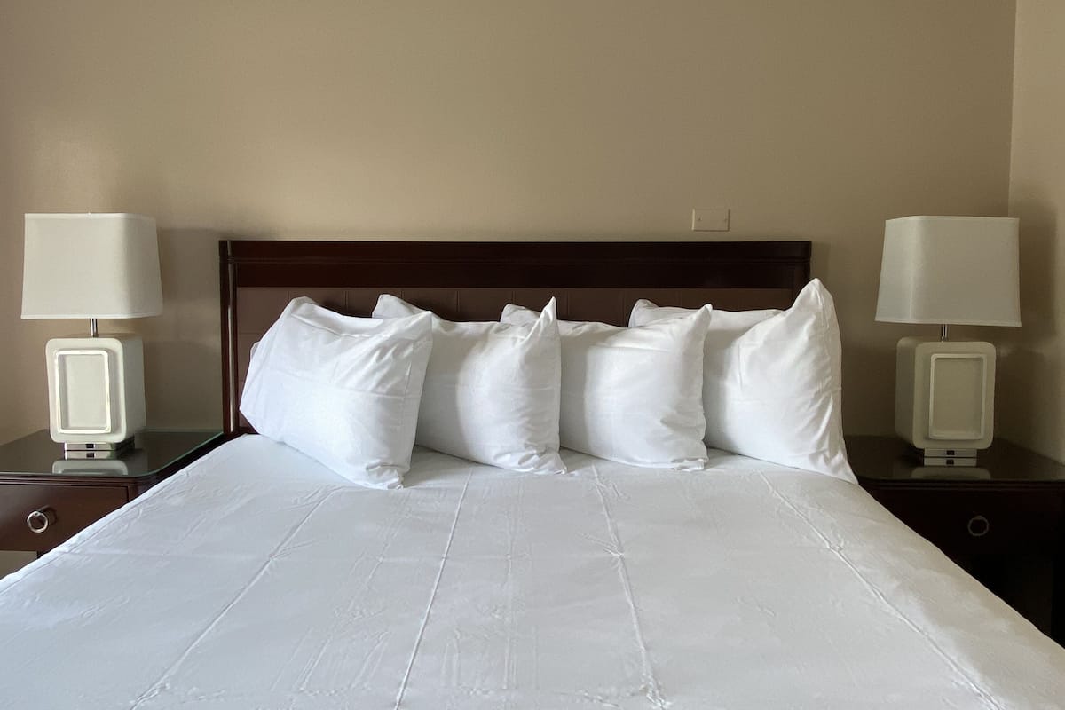 A neatly made bed with white linens and pillows, flanked by two bedside tables with lamps.