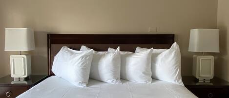 A neatly made bed with white linens and pillows, flanked by two bedside tables with lamps.