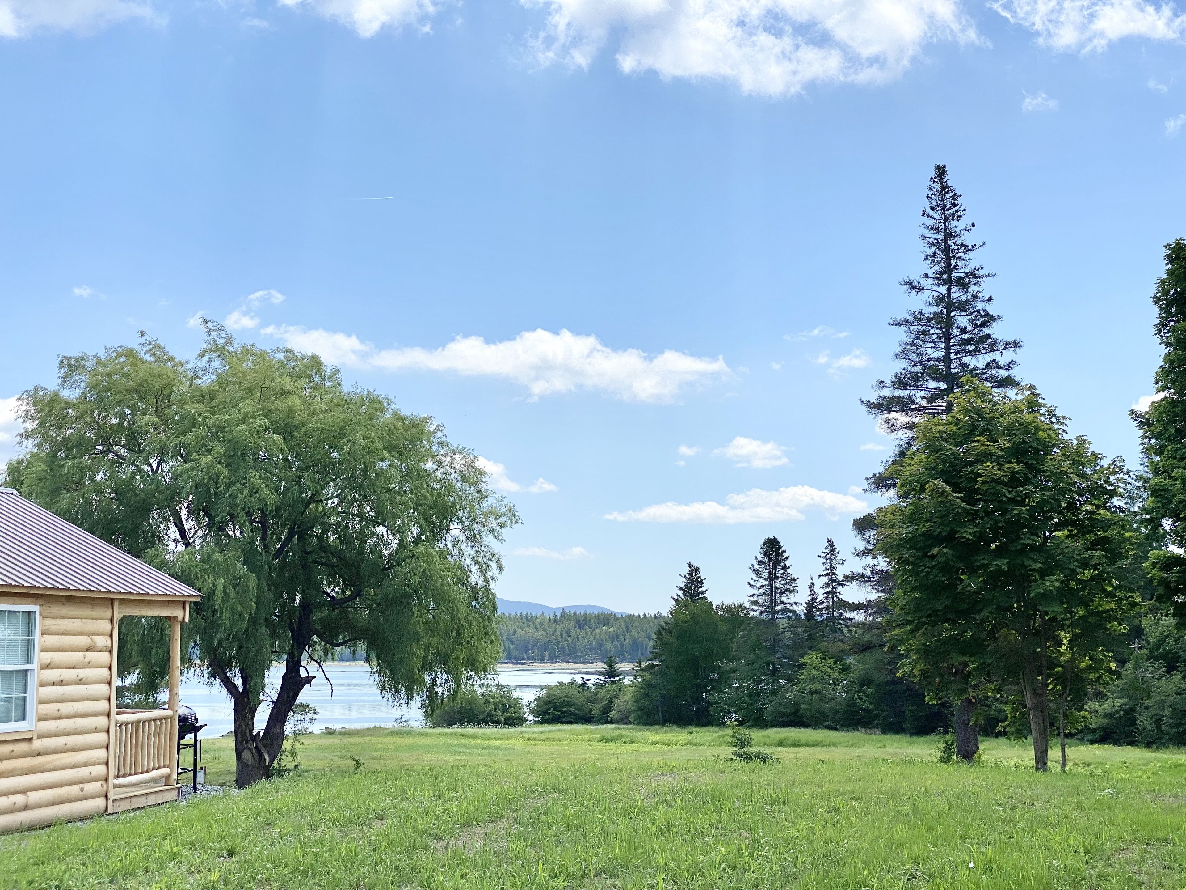 Une cabane en rondins dotée d’une véranda et offrant une vue sur un lac et une forêt.