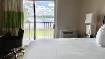 Habitación de hotel con cama, una silla, televisión y vista a un lago a través de una puerta corrediza.