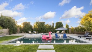 Un patio trasero con piscina, sillas de descanso, un flotador de flamenco y una zona de estar cubierta.