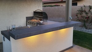 Una cocina exterior con una parrilla, un lavamanos y una encimera.