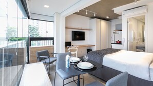 A modern hotel room with a balcony, a dining area, a sofa, a TV, and a kitchenette. - Charlie Itaim Bueno Brandão (São Paulo)