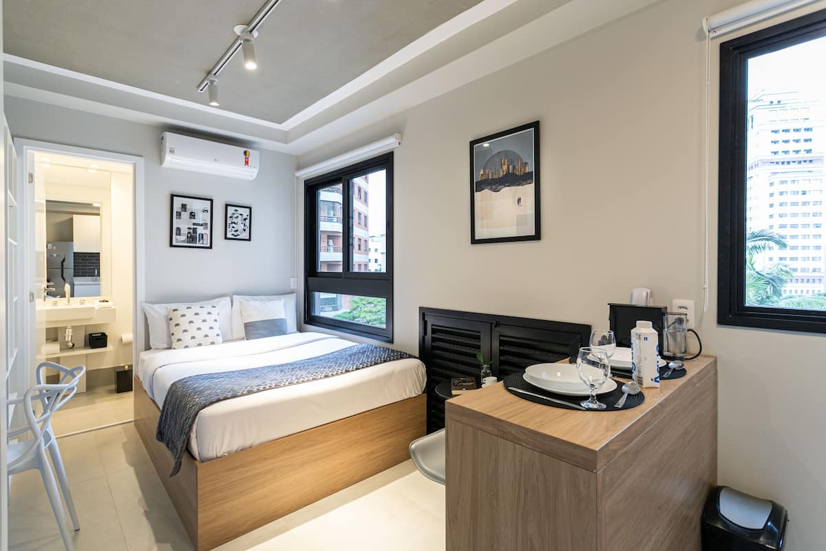 Une chambre d’hôtel moderne, équipée d’un lit, d’une table de chevet et offrant une vue sur la ville par la fenêtre.