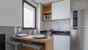 A modern kitchen with a wooden table, two chairs, a refrigerator, a coffee maker, and a window. - Charlie Itaim Bueno Brandão (São Paulo)