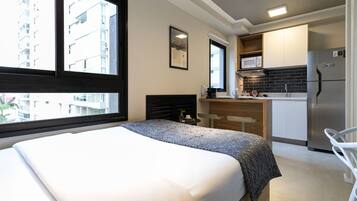 Une chambre d’hôtel avec un lit, une petite kitchenette, un coin repas et une vue sur la ville.