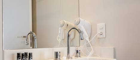 A bathroom with a sink, two hair dryers, and a mirror.