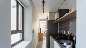 A narrow kitchen with a window, a built-in stove, and a black countertop. - Charlie Itaim Bueno Brandão (São Paulo)