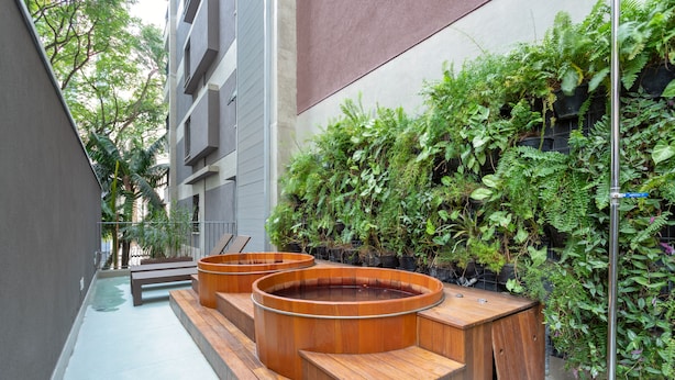 A modern outdoor seating area with wooden benches and planters, surrounded by lush greenery and a building facade. - Charlie Itaim Bueno Brandão (São Paulo)