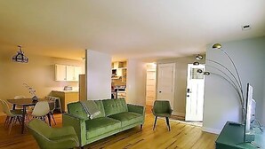 A spacious living room with a green sofa, wooden flooring, and a dining area with a table and chairs.