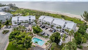 Un hotel frente a la playa con varias construcciones, piscina y estacionamiento.