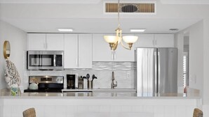 Una cocina moderna con armarios blancos, electrodomésticos de acero inoxidable y una isla central con asientos.