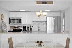 Una cocina moderna con armarios blancos, electrodomésticos de acero inoxidable y una isla central con asientos.