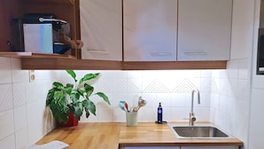 Una cocina con armarios blancos, encimera de madera, un fregadero, una planta y un portalapices.