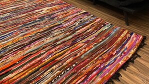 Une pièce avec un fauteuil en cuir vert, un canapé noir et un tapis coloré tissé.