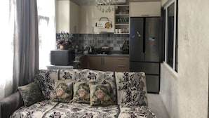 Een moderne keuken met een koelkast, magnetron en een kroonluchter. Er is een bank met bloemenkussens en een raam met gordijnen.