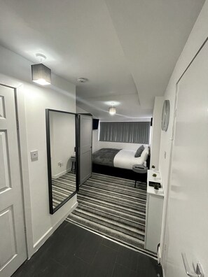 Une chambre d’hôtel comprenant un lit, une table de chevet, un miroir, une armoire et un sol recouvert de moquette.